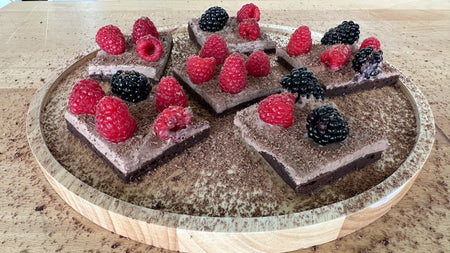 Schokoschnitten mit Schokoladencreme, dekoriert mit frischen Himbeeren und Brombeeren, auf einem runden Holztablett serviert.