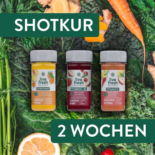 Drei Flaschen LiveFresh Shots auf einem Hintergrund aus frischem Blattgemüse, Karotten und Süßkartoffeln. Die Sorten sind „Kurkuma Power“ mit Curcumin, „Sunshine Berry“ mit Vitamin D3 + K2 und „Ingwer Sturm“ mit Vitamin C. Oben steht „SHOTKUR“, unten „2 WOCHEN“.
