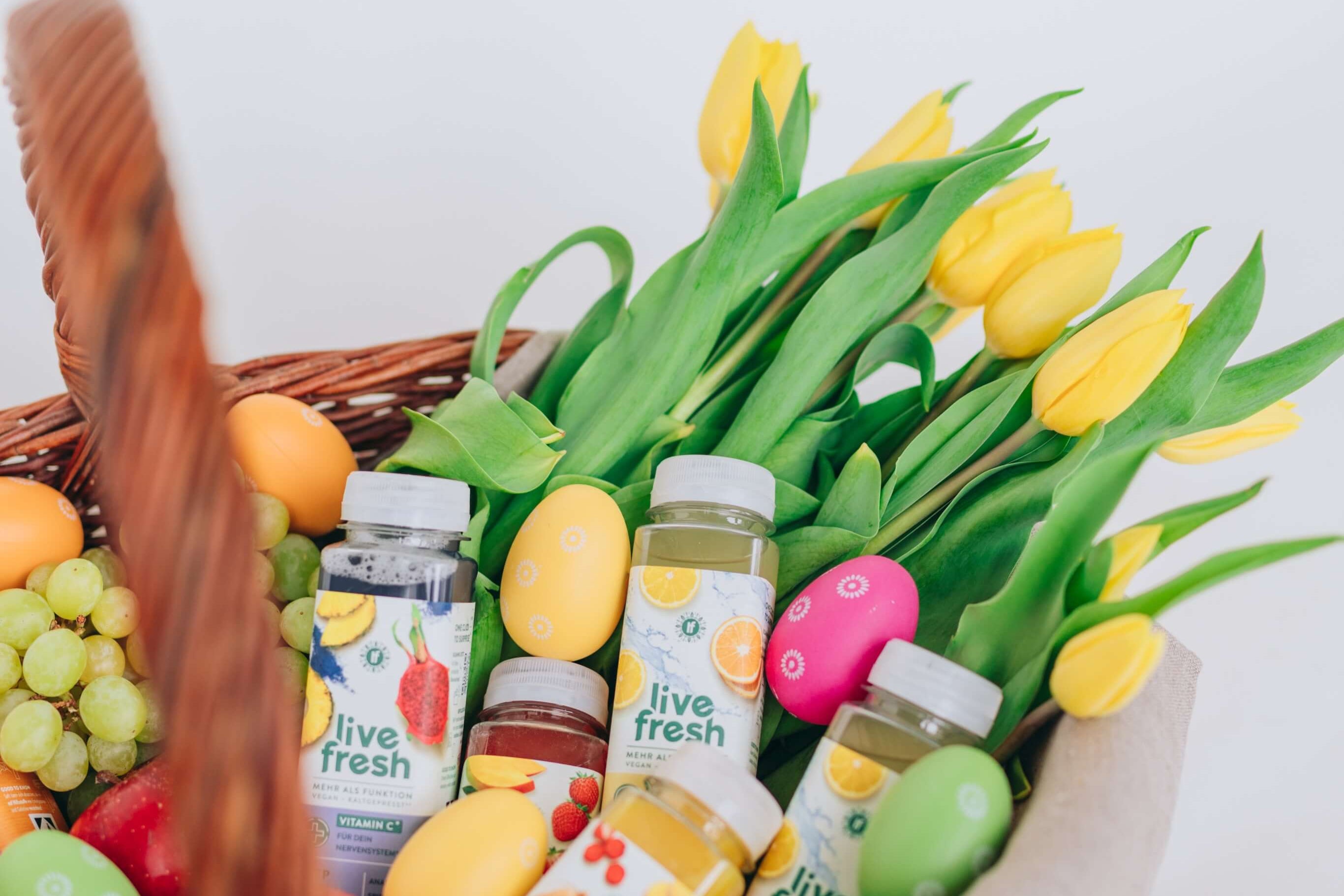 Osterkorb mit verschiedenen LiveFresh Säften, Ostereiern, Trauben und gelben Tulpen.