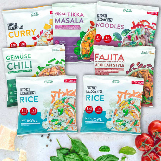 Flatlay mit sieben LiveFresh Tiefkühlgerichten, darunter High Protein Curry, Vegan Tikka Masala, Gemüse Chili, Fajita Mexican Style, High Protein Noodles und zwei High Protein Rice Varianten. Umgeben von frischem Spinat, Tomaten und Parmesanstücken.