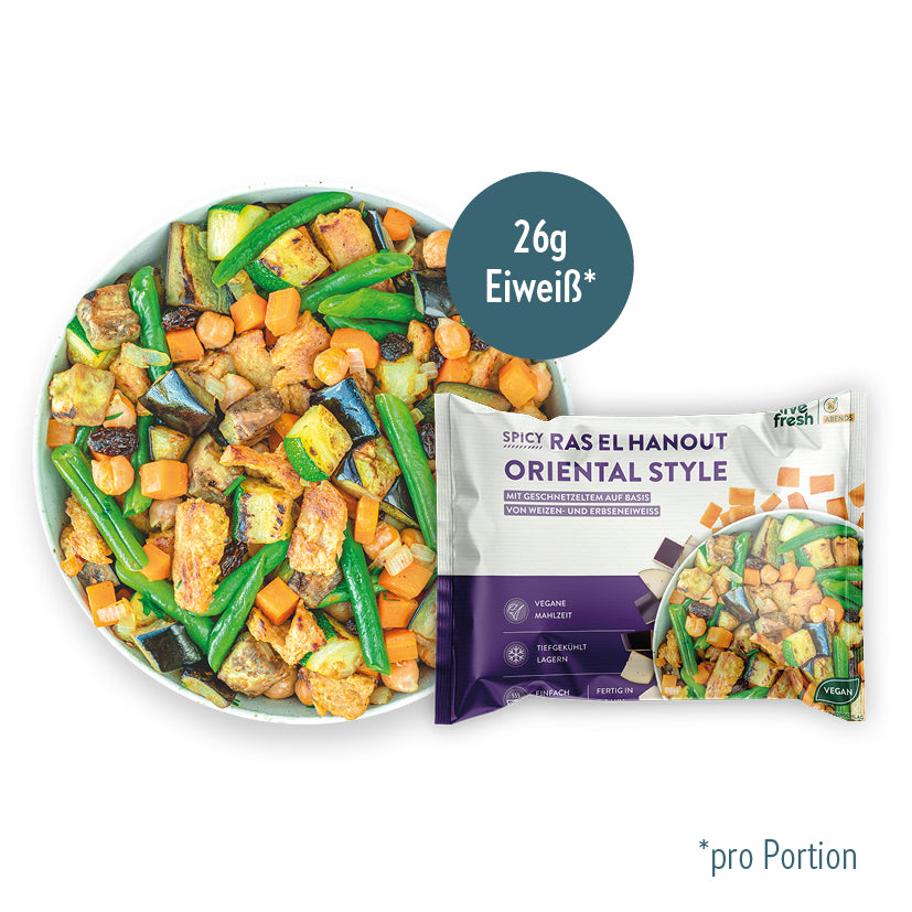 LiveFresh "Spicy Ras El Hanout Oriental Style" Tiefkühlgericht mit Aubergine, Karotten, grünen Bohnen, Kichererbsen, Rosinen und pflanzlichem Geschnetzeltem, serviert in einer weißen Schüssel. Daneben die Produktverpackung mit violettem Design und einem Hinweis auf 26g Eiweiß pro Portion.