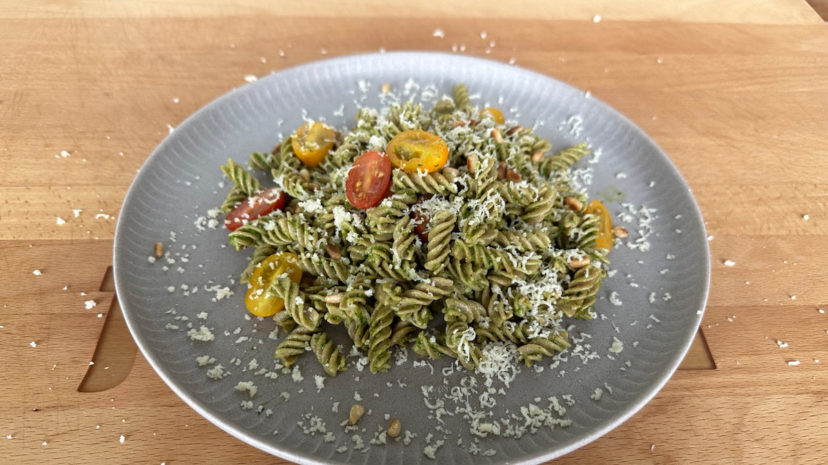 Ein Teller Fusilli-Pasta mit grünem Bärlauchpesto, garniert mit halbierten Kirschtomaten und geriebenem Parmesan.