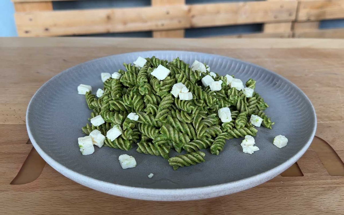 Ein Teller mit grünen Pesto-Fusilli garniert mit gewürfeltem Feta-Käse, serviert auf einem hölzernen Tisch.