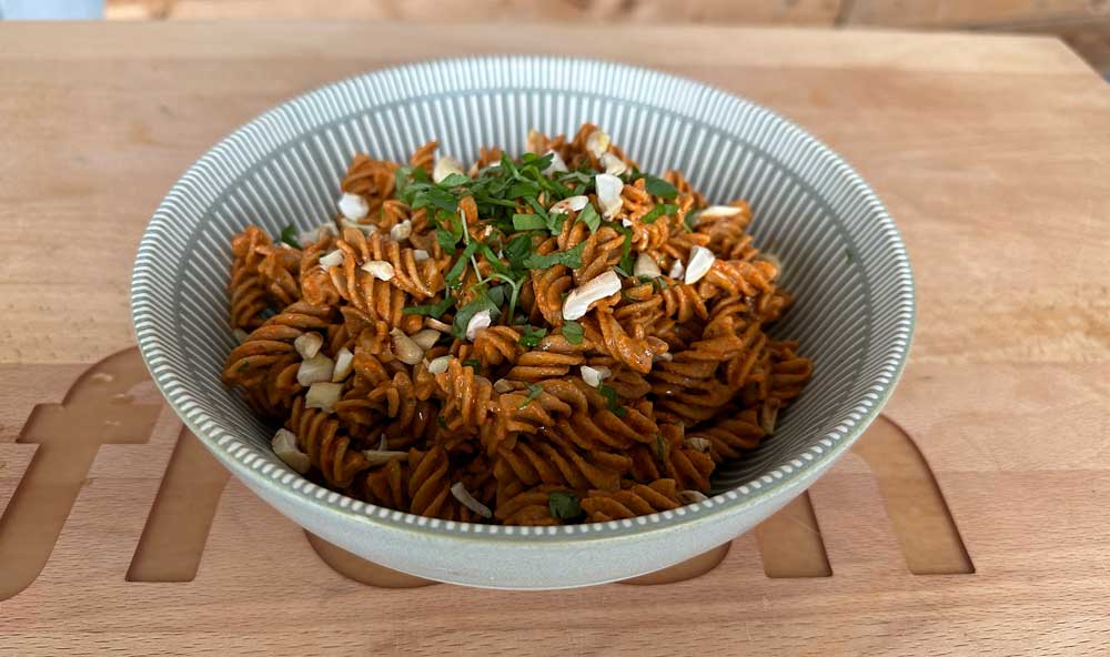 Gekochtes Fusilli Rezept in einer geriffelten grauen Schüssel, garniert mit frischen Kräutern und gehackten Nüssen, serviert auf einem Holzbrett.