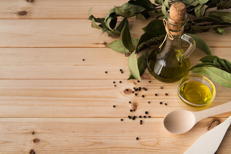 Flasche Oregano Öl auf Holztisch mit Lorbeerblättern. Fokus auf die Wirkung, Anwendung und sichere Einnahme des Öls, das nicht krebserregend ist.