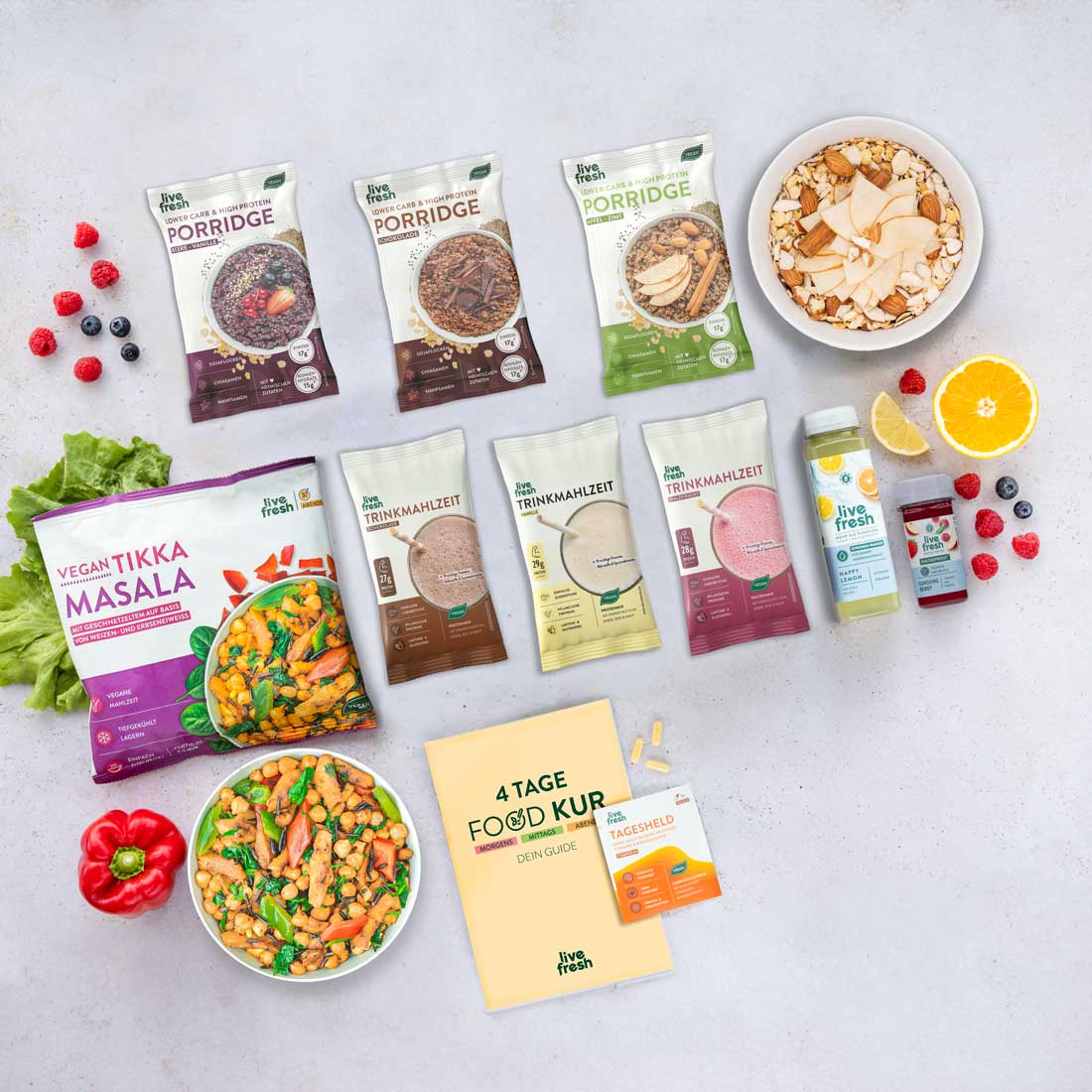 Sortiment an Produkten der Marke LiveFresh, die Teil eines 4-tägigen Foodkur-Plans sind. Zu sehen sind Porridge-Packungen in verschiedenen Geschmacksrichtungen, Trinkmahlzeiten, ein veganes Tikka-Masala-Fertiggericht mit einer Schüssel angerichteter Mahlzeit, Obst, Smoothie-Flaschen, sowie ein Guide-Heft und Nahrungsergänzungsmittel. 