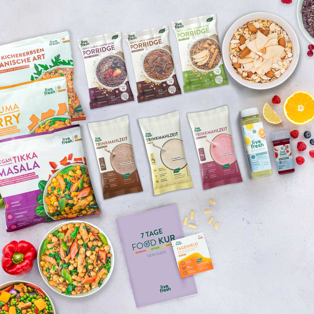 Verschiedene Produkte einer 7-Tage-Food-Kur von LiveFresh, darunter Fertiggerichte, Trinkmahlzeiten, Porridge, Säfte und Vitamine. Daneben liegen Zitronen, Himbeeren, Blaubeeren und Paprika. 