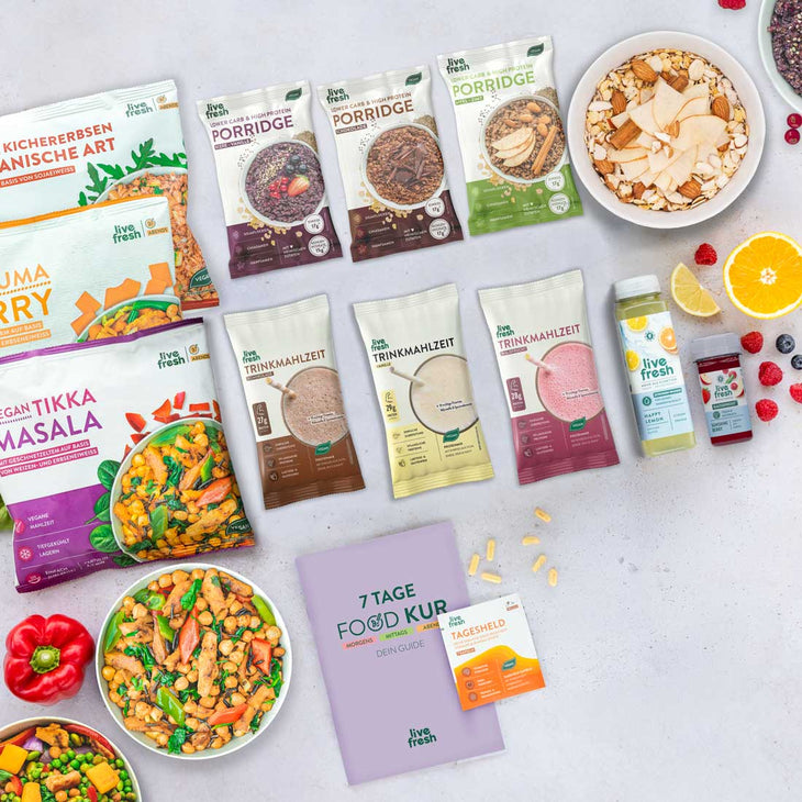 Verschiedene Produkte einer 7-Tage-Food-Kur von LiveFresh, darunter Fertiggerichte, Trinkmahlzeiten, Porridge, Säfte und Vitamine. Daneben liegen Zitronen, Himbeeren, Blaubeeren und Paprika. 