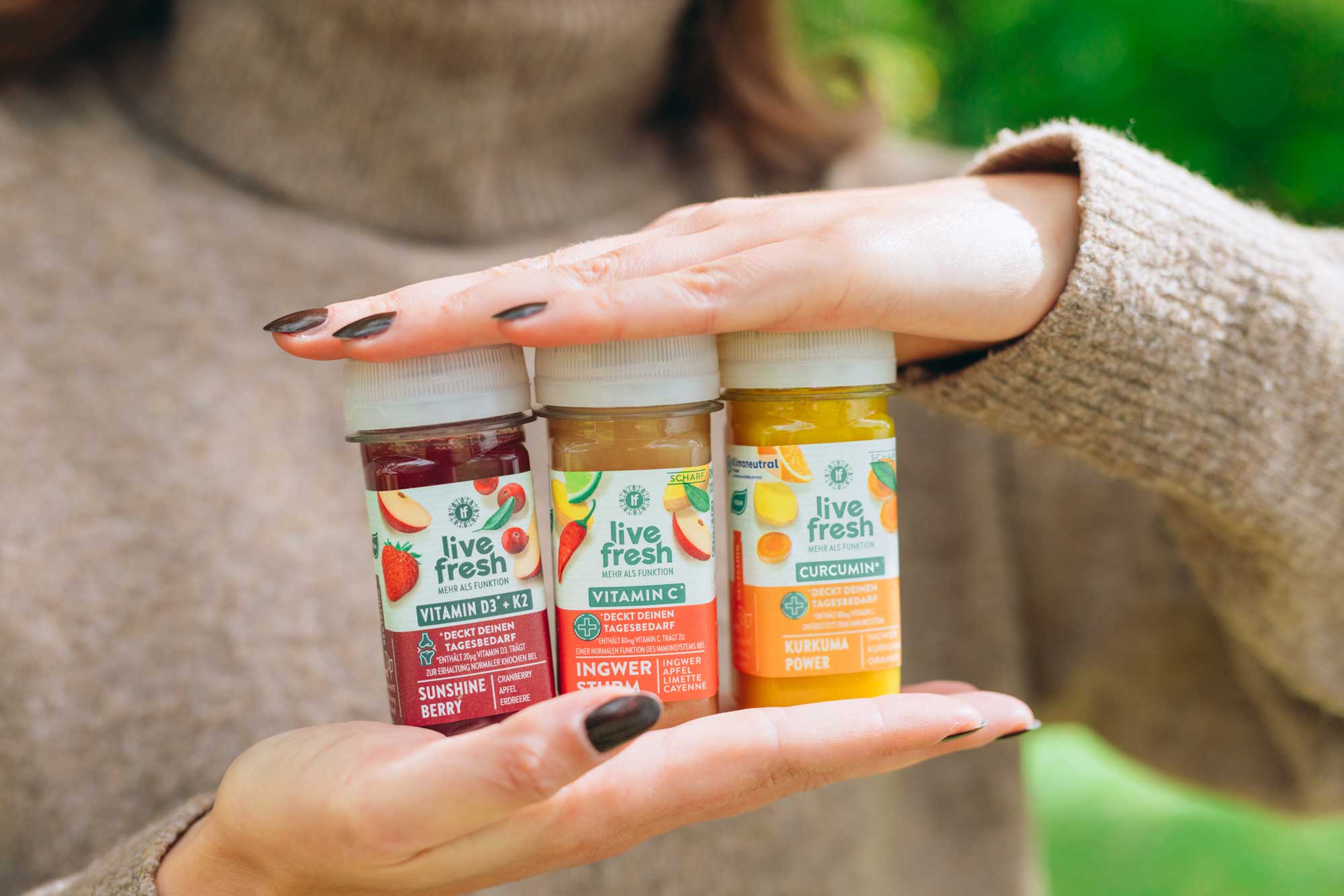 Eine Person hält drei LiveFresh-Shots in drei verschiedenen Geschmacksrichtungen in den Händen. Der Kopf ist nicht zu sehen. 