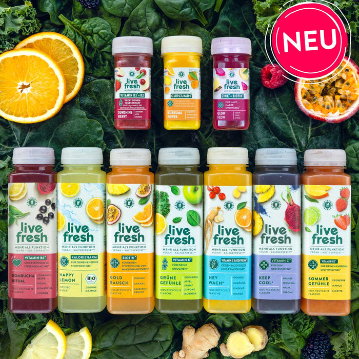 7 verschiedene Säfte und 3 Shots von LiveFresh, im Hintergrund sind Spinat- und Kohlblätter zu sehen wie andere Früchte. Rechts oben ist ein Hinweis mit "NEU" zu sehen. 